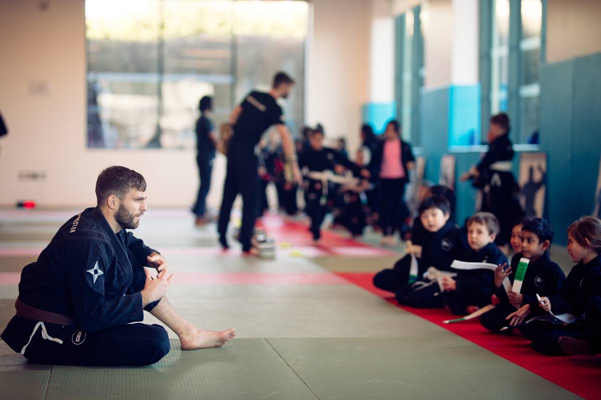 Cubs-age children sitting along the mat with their instructor kneeling in front of them