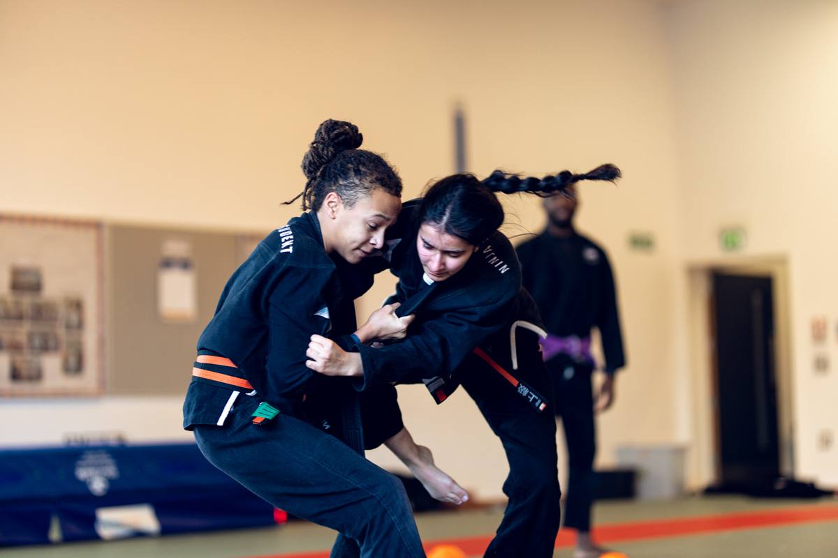 Two Kaizen students grappling while an instructor watches